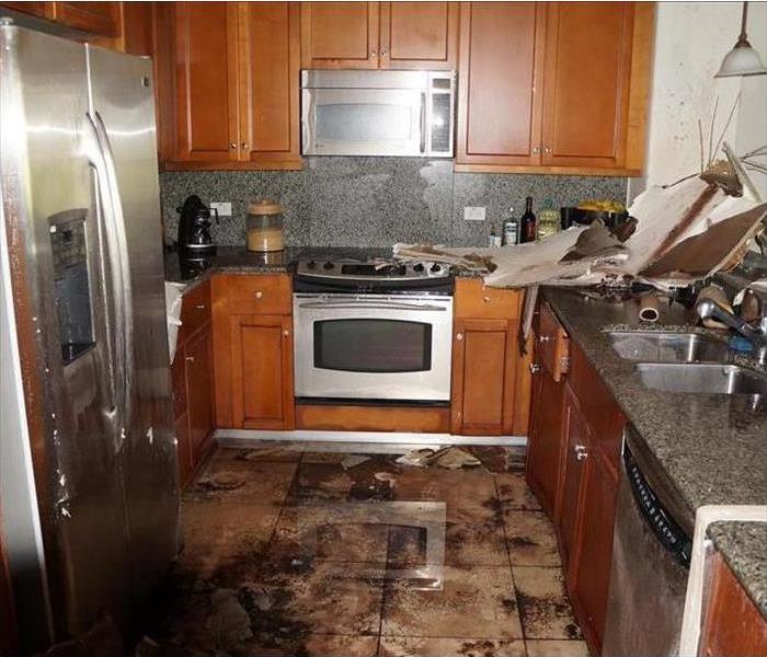 Kitchen with water damage on the floor and messy cabinetry.