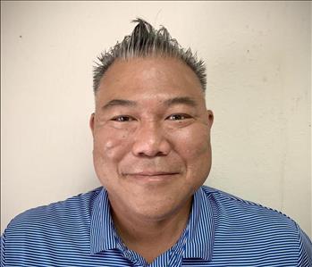 Male employee standing in the front of the tan background, smiling