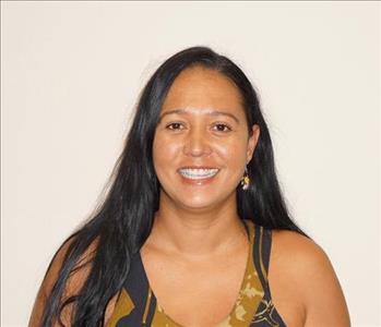 Female employee standing in the front of the tan background, smiling