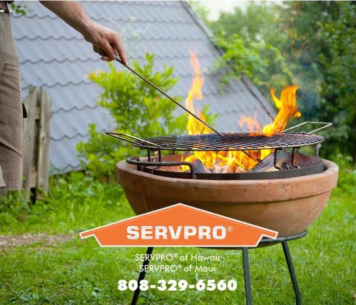 A person is grilling on a charcoal barbeque in a backyard. 