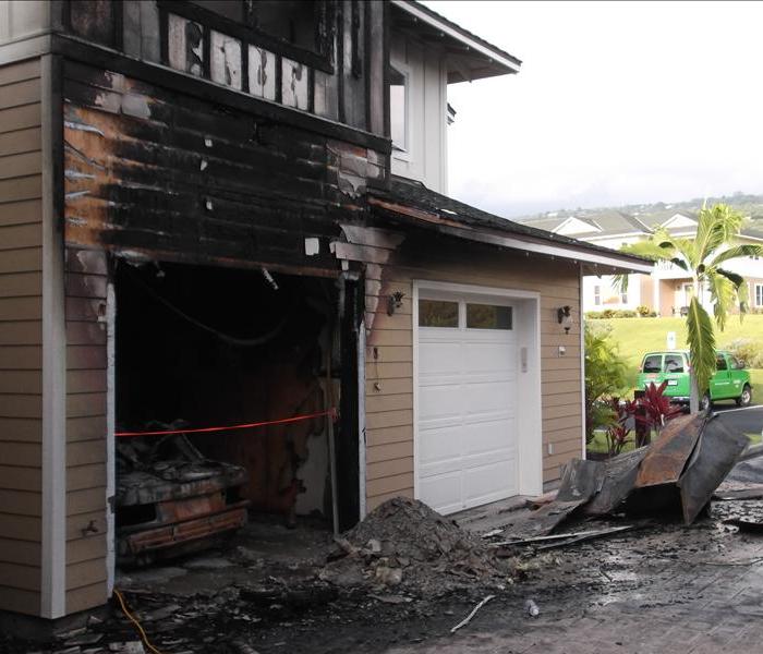 Front of the house with fire damaged garage door and a burnt mercedes inside