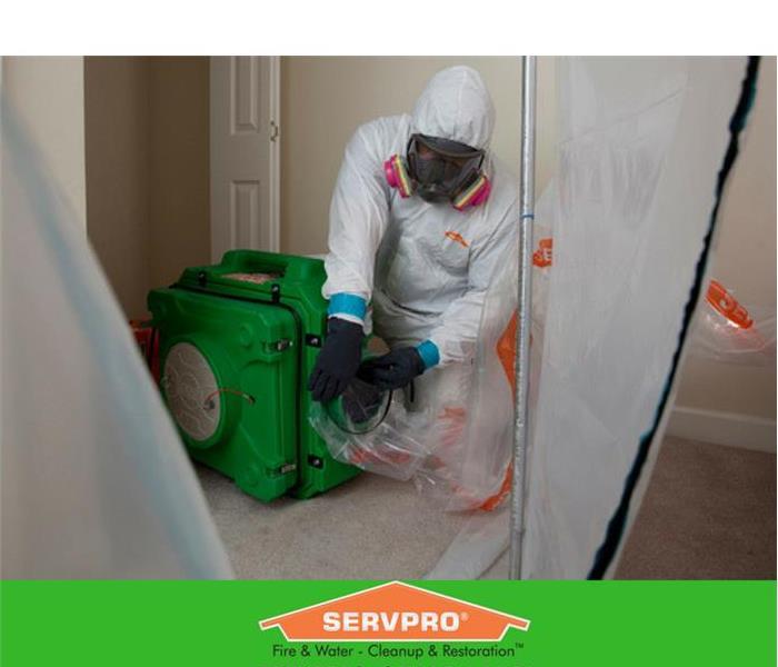 Man in a hazmat suit putting a plastic sleeve on an air cleaner in an apartment.