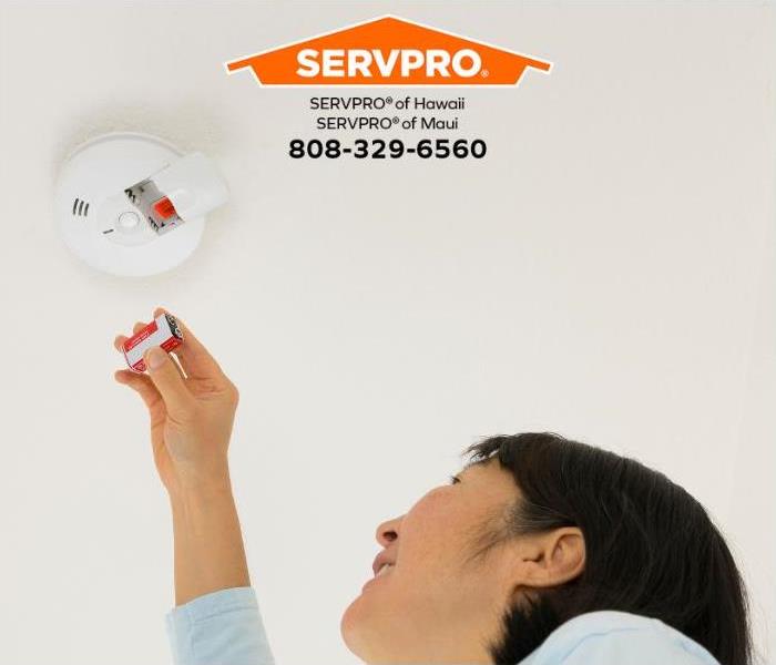 A person replaces the battery in a smoke detector.